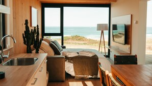 A modern interior with a kitchen, a seating area with a view of the ocean, and a flat-screen TV mounted on the wall.