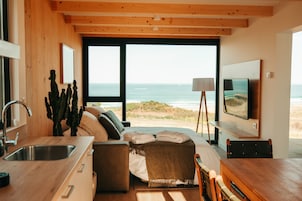 Un interior moderno con cocina, zona de estar con vista al océano y televisor de pantalla plana montado en la pared.