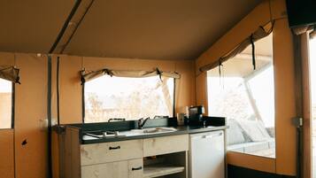 A compact kitchen with a sink, stove, and storage cabinets. There is a window providing natural light and a view of the outdoors.