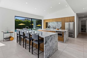 A modern kitchen with a marble island, stainless steel appliances, and a large window overlooking a garden.