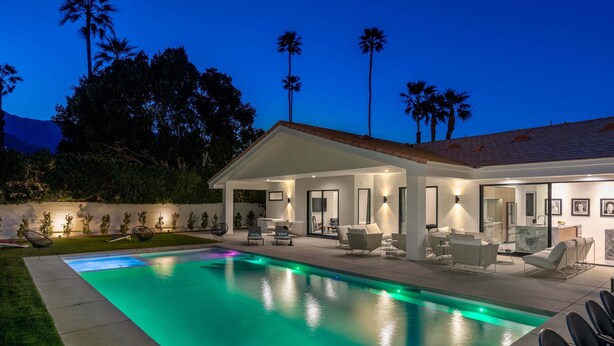 Una casa moderna con piscina, mobiliario de exterior y palmeras.