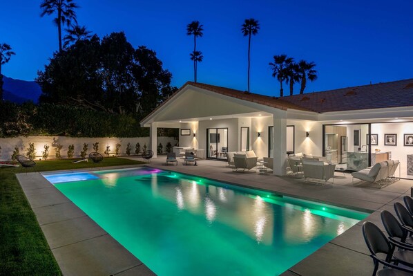 A modern house with a swimming pool, outdoor furniture, and palm trees.