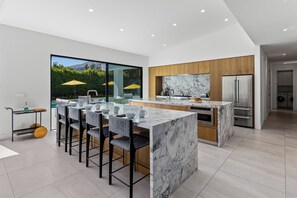 A modern kitchen with a marble island, wooden cabinets, and a stainless steel refrigerator.
