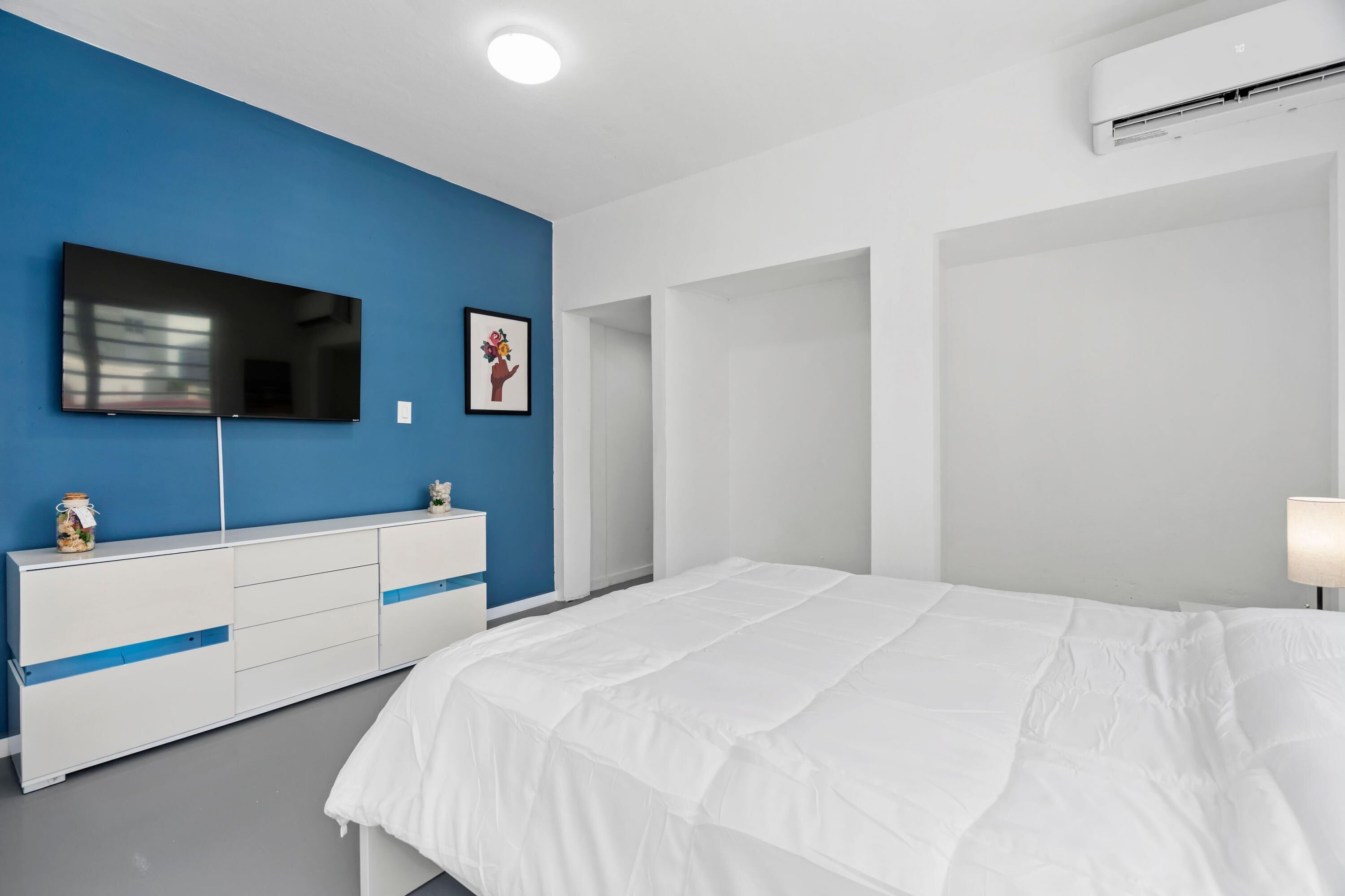 Ein Schlafzimmer mit einem großen Bett, einem an der Wand montierten Fernseher, einem Schminktisch und einem gerahmten Bild.