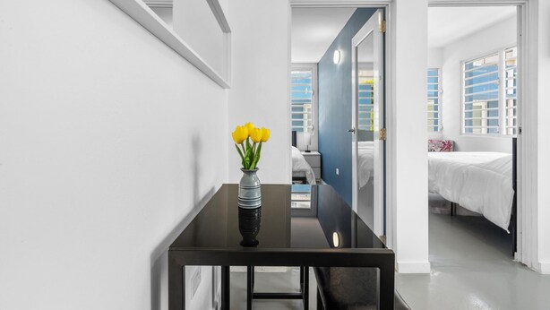 Une chambre d’hôtel moderne avec une table en verre, un vase rempli de fleurs jaunes et une vue sur la ville par la fenêtre.