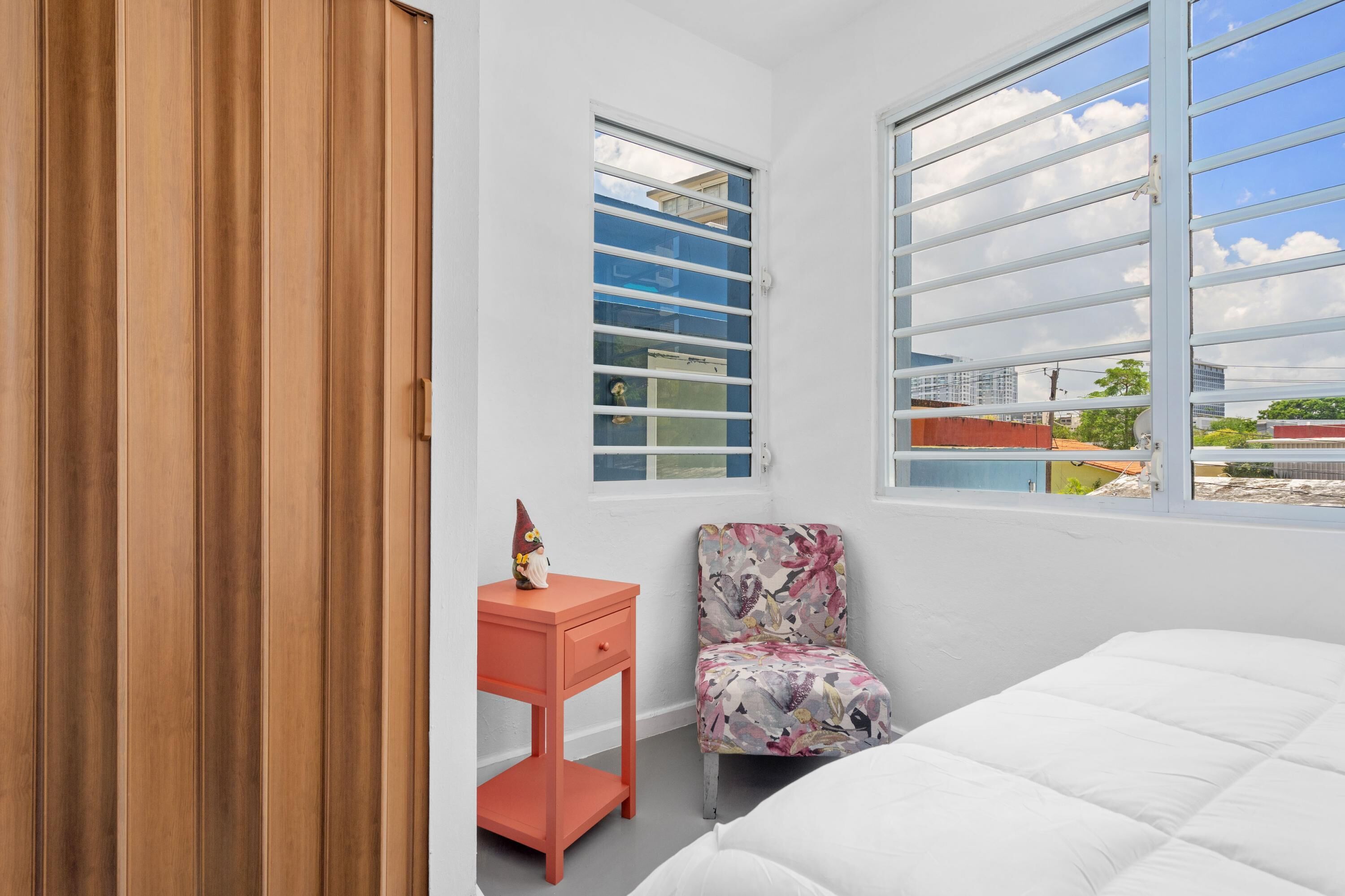A bedroom with a bed, a chair, a desk, and two windows.