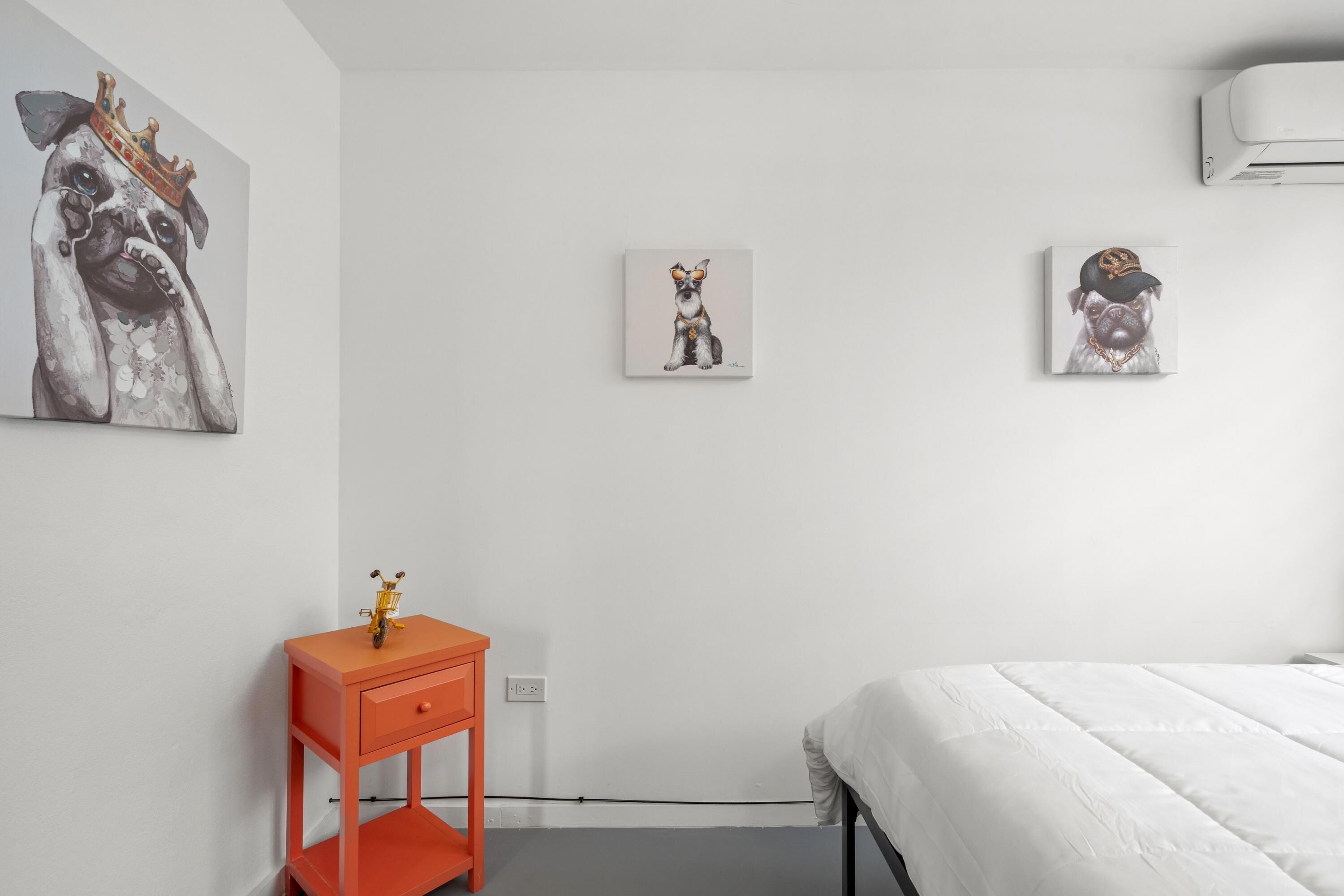 A bedroom with a bed, a nightstand, and three wall-mounted paintings of dogs.