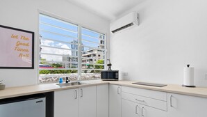 Une cuisine moderne avec des armoires blanches, un four à micro-ondes encastré et une fenêtre donnant sur des bâtiments et des espaces verts.