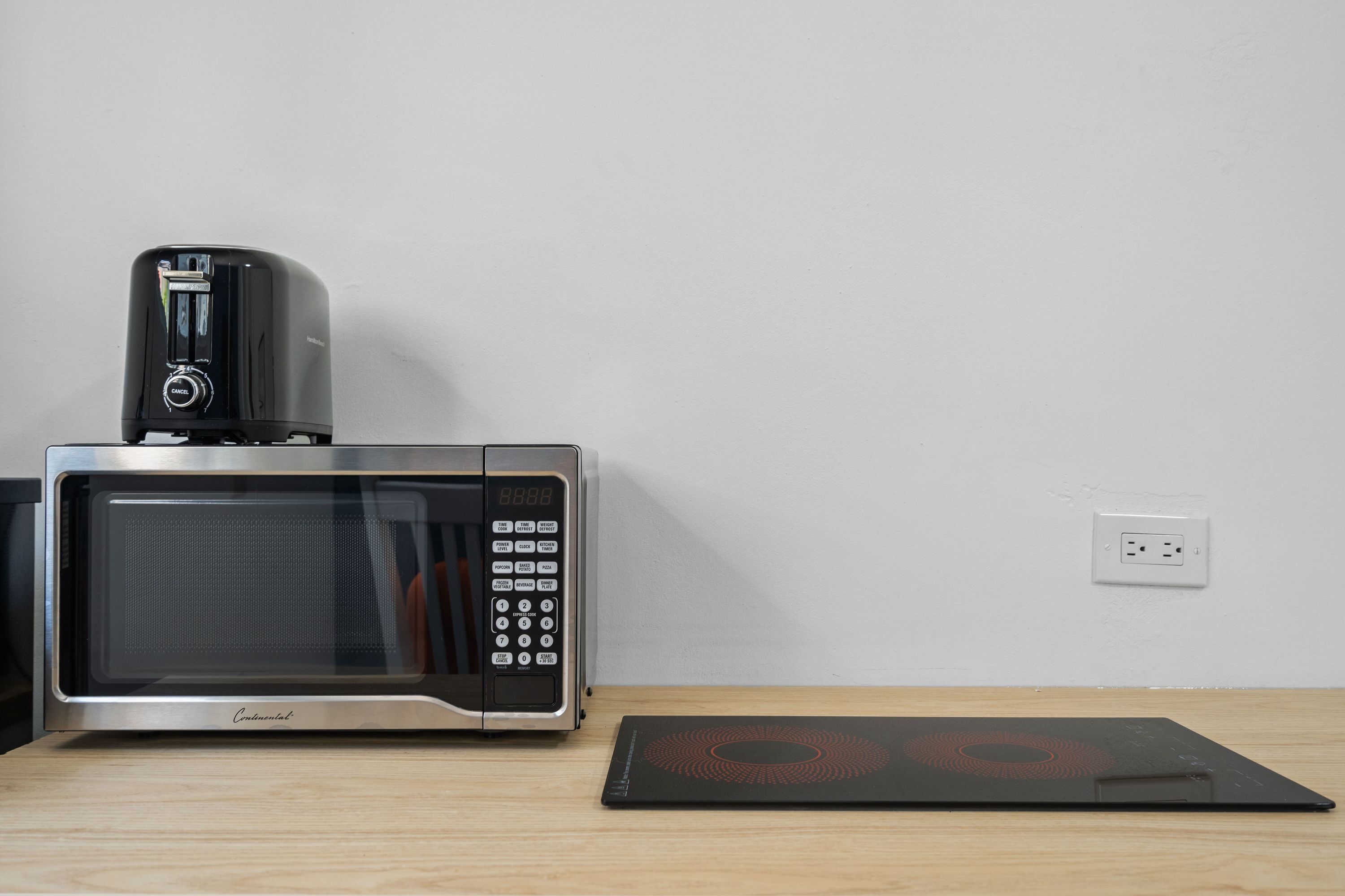 Forno de micro-ondas com visor digital e painel de controle, colocado sobre uma superfície de madeira ao lado de uma tomada.