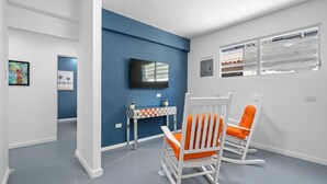 A room with a blue accent wall, a television mounted above a small table, and two rocking chairs with orange cushions. - Otium Rentals Condado Space Near Attractions (San Juan)
