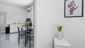 Une cuisine moderne avec des meubles blancs, un plan de travail noir et une table à manger en verre, accompagnée de chaises. Un tableau encadré orne le mur, et un vase rempli de fleurs est posé sur une petite table.