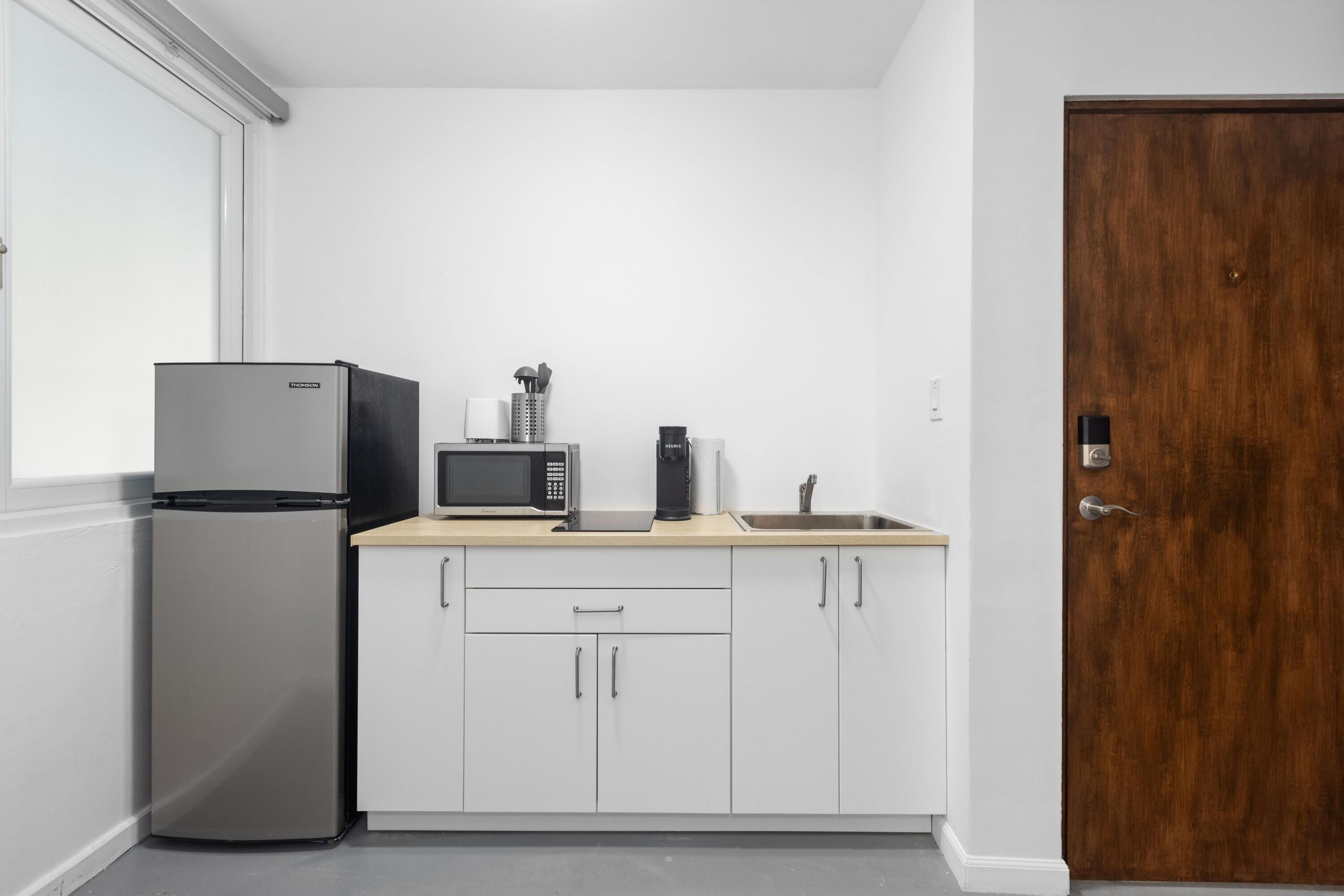 A compact kitchen with white cabinets, a stainless steel refrigerator, a microwave, and a coffee maker on the countertop.