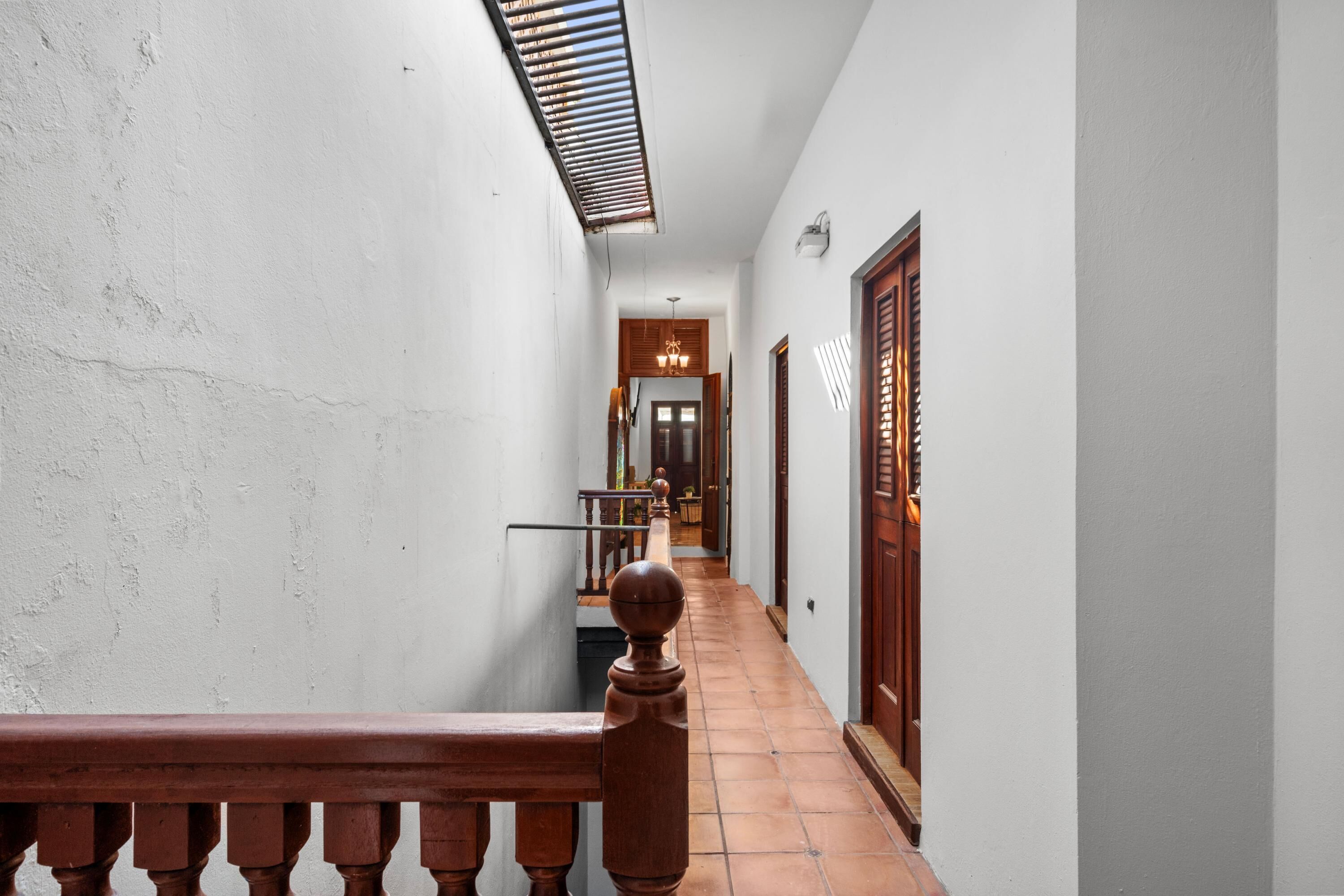 A narrow hallway with a wooden railing, a tiled floor, and a ceiling vent.