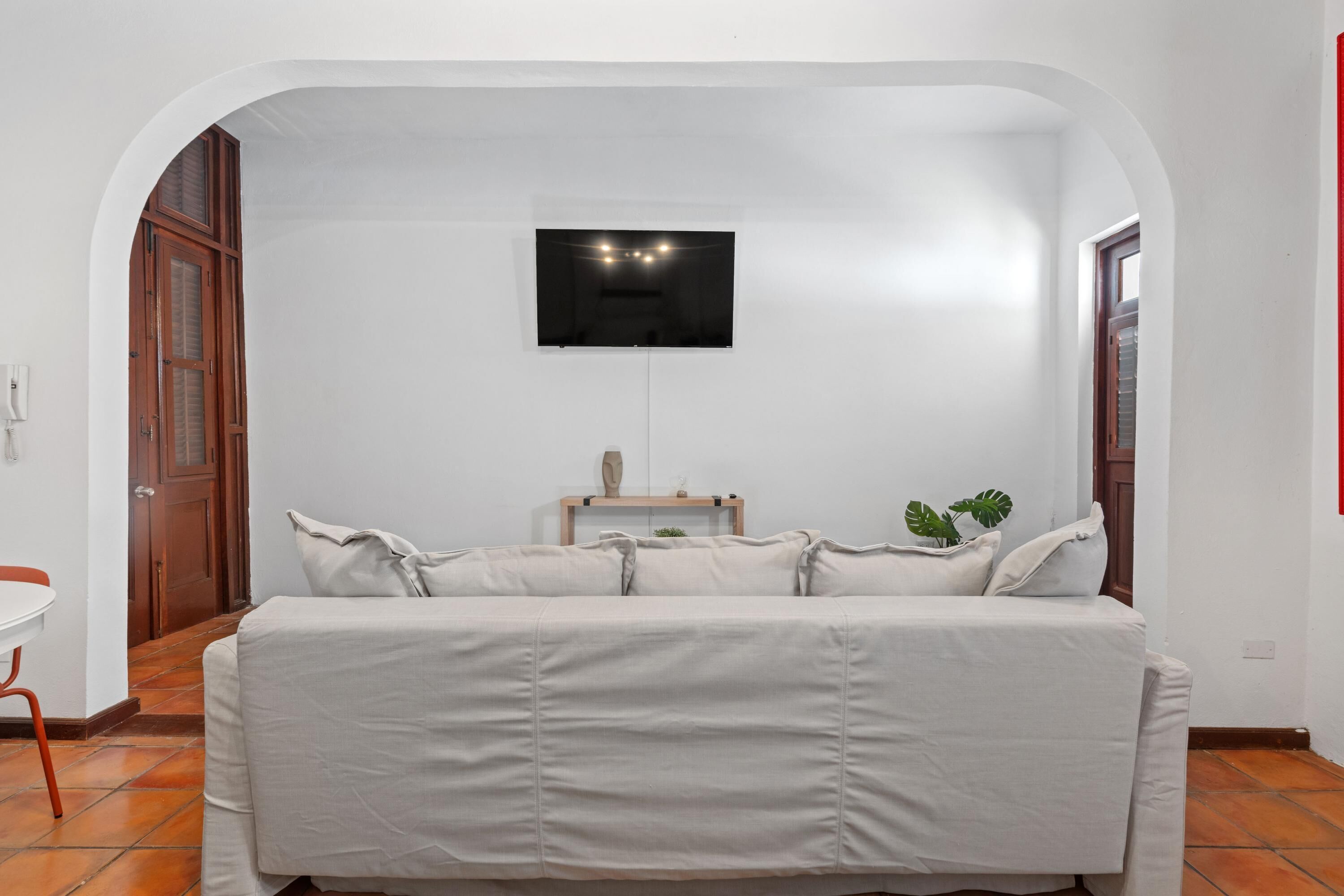 Une pièce avec un canapé blanc, une petite table et un téléviseur fixé au mur.