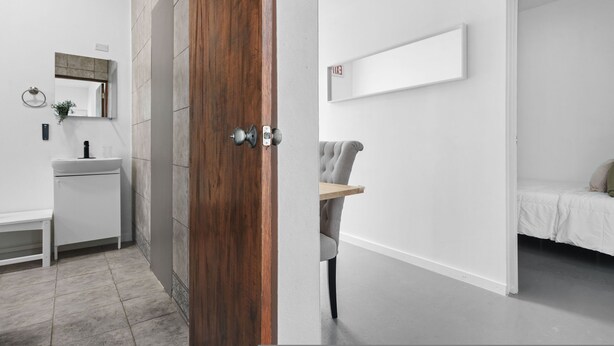 A modern bathroom with a wooden door, a white sink, and a mirror. - Otium Rentals Spacious Apartment in Condado (San Juan)