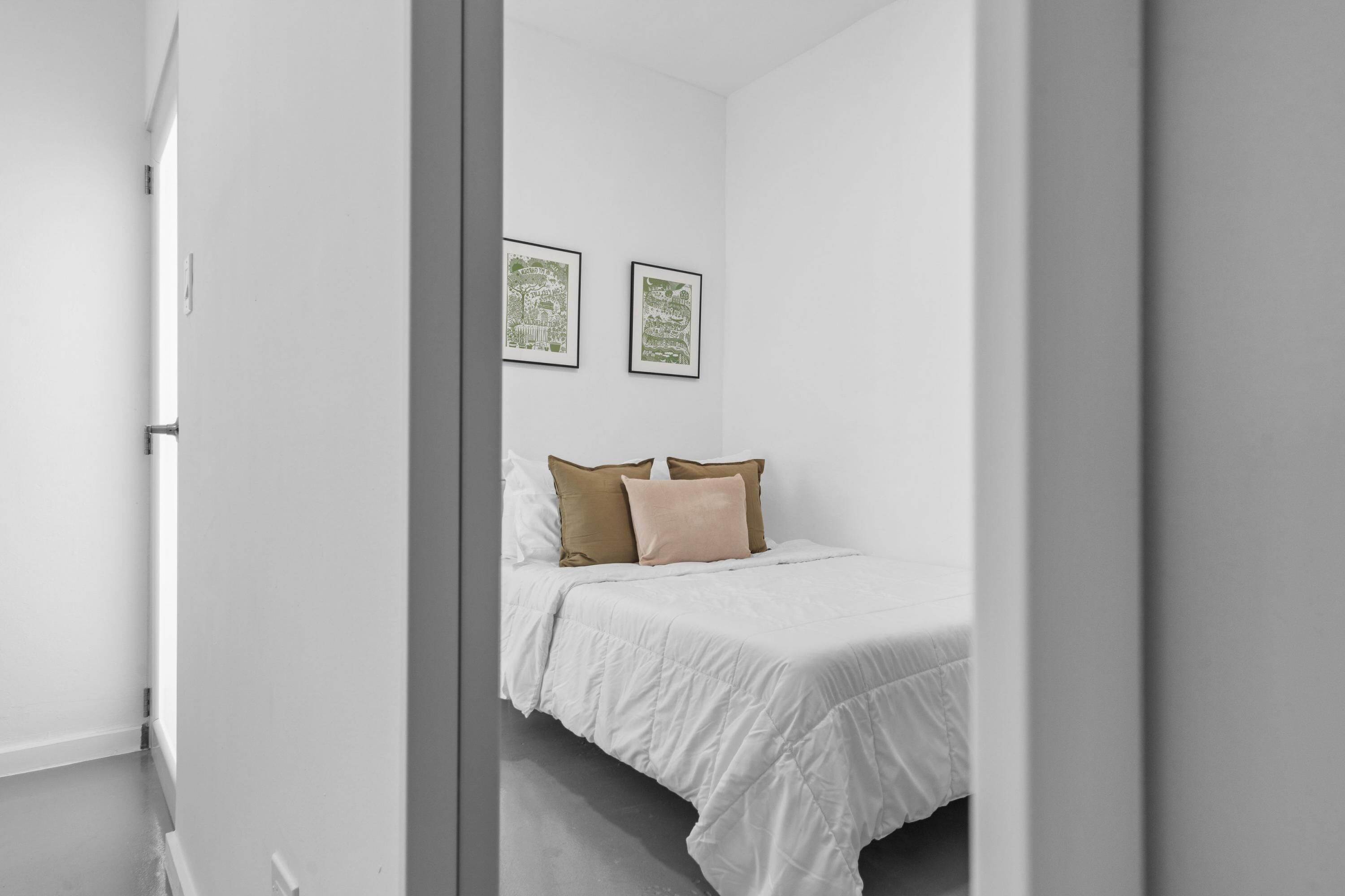 A minimalist bedroom with a bed, white walls, and two framed pictures.