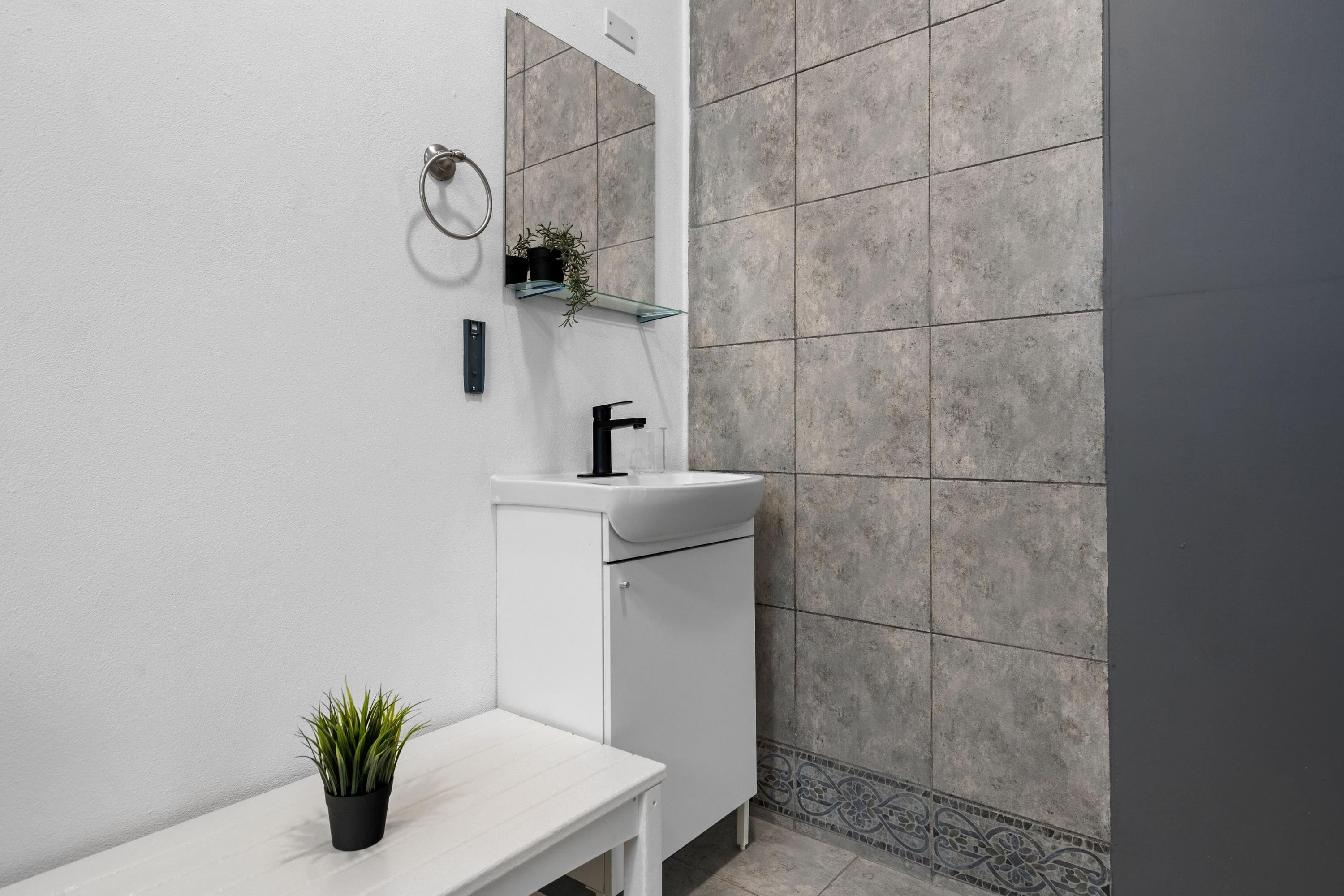 A modern bathroom with a white vanity, a black sink, a mirror, and a potted plant.