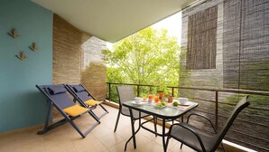 A balcony with a dining table, two lounge chairs, and a view of greenery. - Urban Bloom Oasis - Mini Zen Maison (Kalamata)