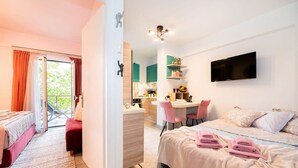 A modern hotel room with a balcony, a kitchenette, a dining area, and a bed with neatly folded towels. - Urban Bloom Oasis - Mini Zen Maison (Kalamata)