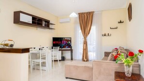 Una sala de estar moderna con televisor, comedor y un sofá con un jarrón de flores.