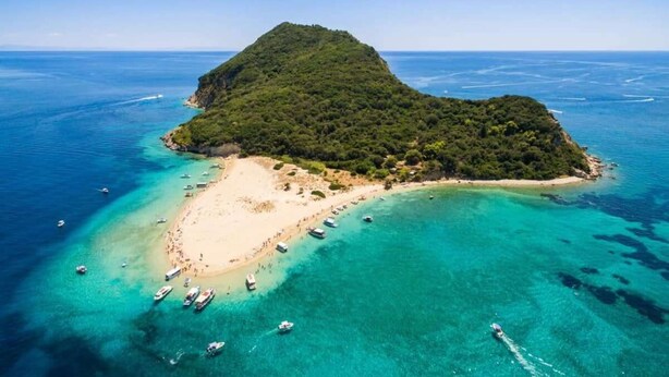 Vista aérea de una pequeña isla con playa y aguas turquesas cristalinas.