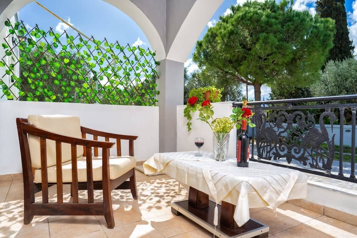 A patio with a wooden chair, a table with a white tablecloth, a wine glass, and a vase with flowers.