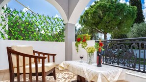 Un patio con una silla de madera, una mesa con mantel blanco, una copa de vino y un florero con flores.