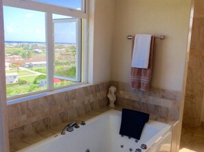 A bathroom with a bathtub, a window with a view of a residential area, and a towel rack with two towels. - Remarkable 3-bed Villa in Christ Church (Providence)