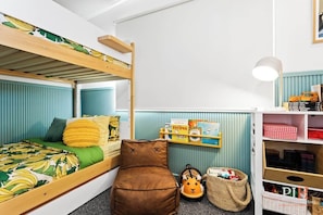 A bunk bed with a green and yellow banana-themed bedspread, a brown cushion, and a shelf with children's books and toys. - Stunning Cape Woolamai House with Private Pool (Cape Woolamai)