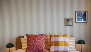Una habitación de hotel con una cama, papel tapiz a rayas y dos cuadros en la pared.