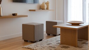 A modern living room with a flat-screen TV, wooden shelves, two grey ottomans, a wooden coffee table, and a patterned rug. - Athenian Hillside Residence (Athens)