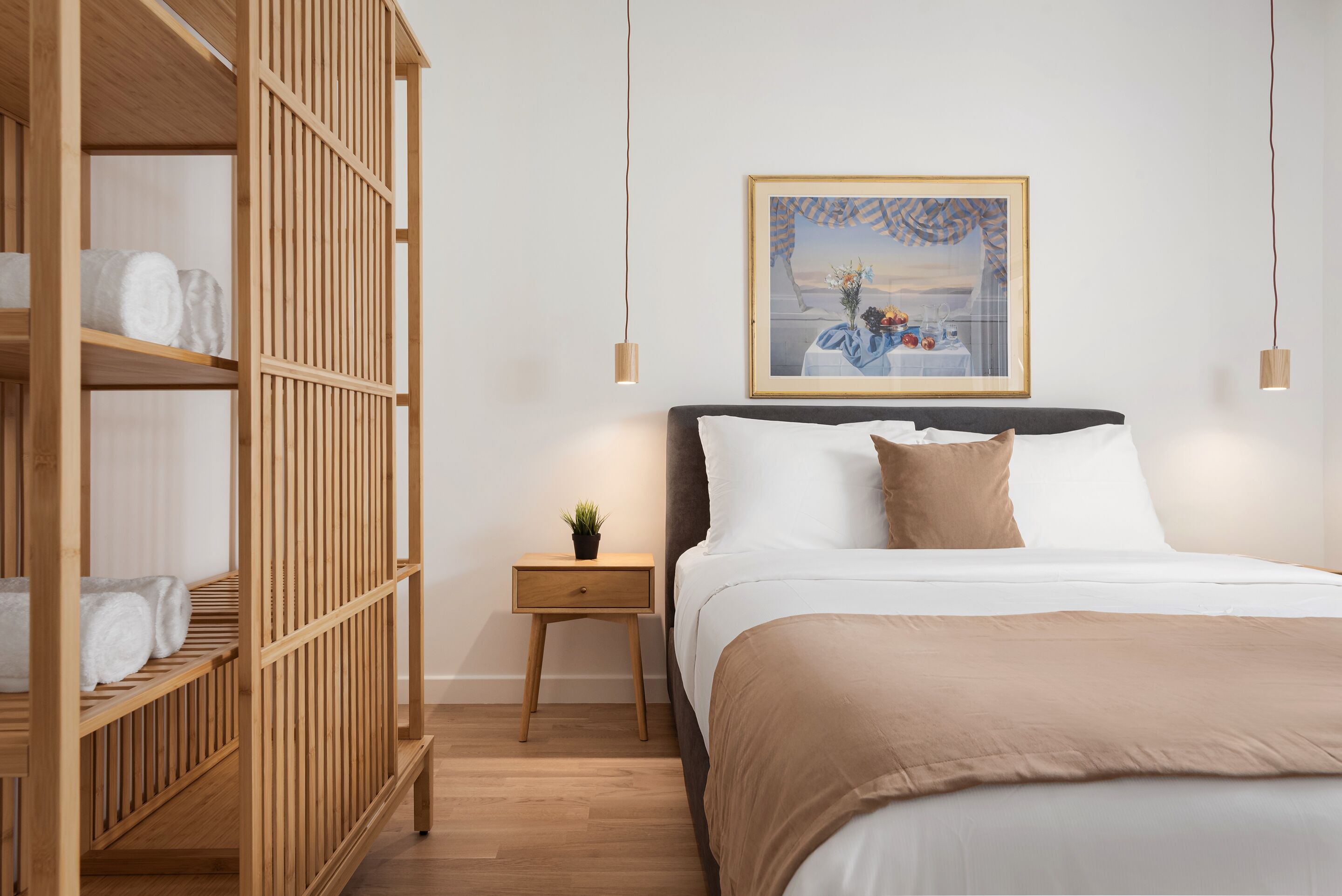 Ein Schlafzimmer mit einem Bett, einem Holzschrank, einem Nachttisch mit Pflanze und einem gerahmten Bild an der Wand.