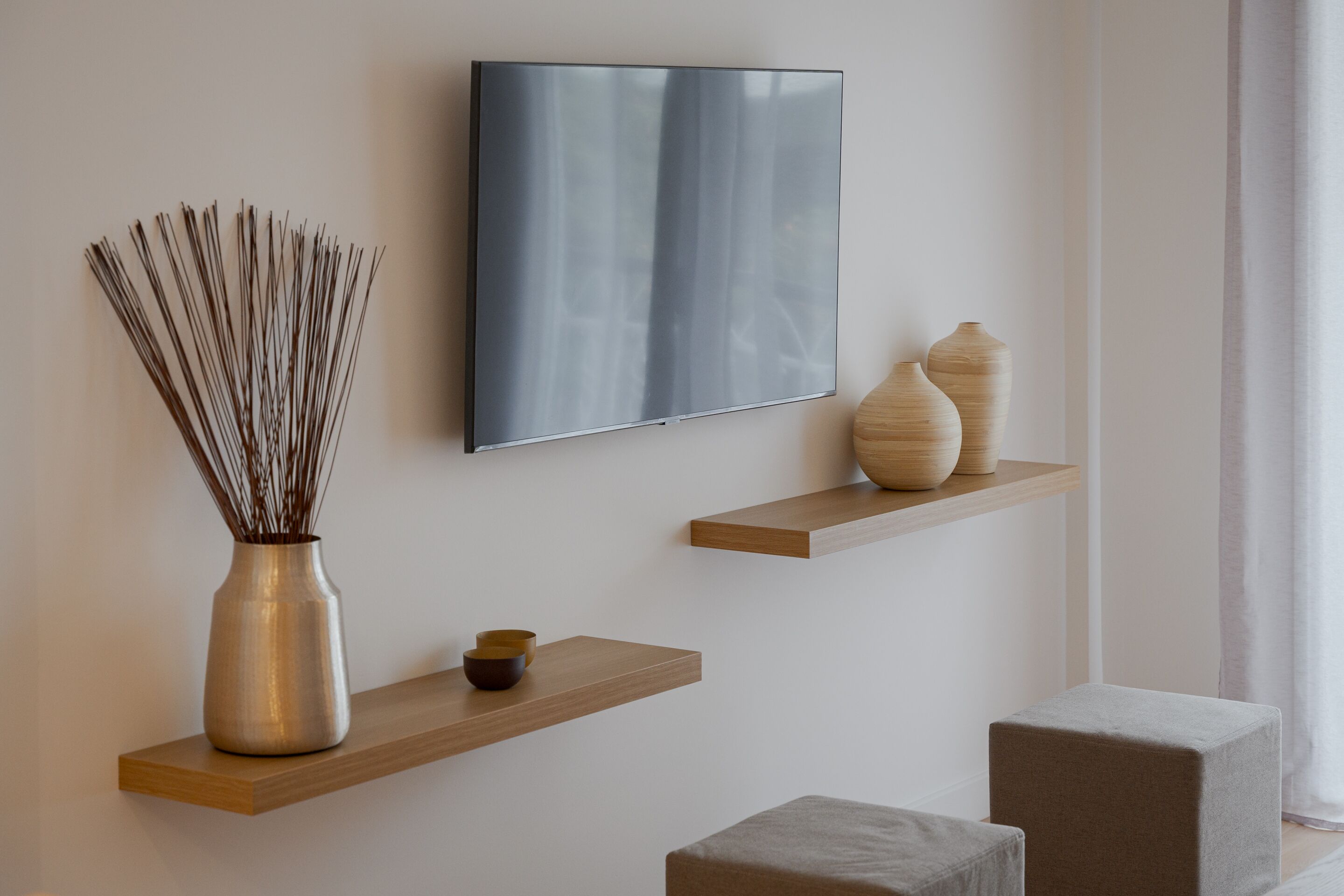 Een moderne woonkamer met een flatscreen televisie aan de muur, houten planken met decoratieve objecten, en een minimalistisch design.