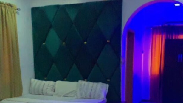 A bedroom with a bed, a dark headboard, and patterned carpet. - Blue Moon Hotel Victoria Island (Lagos)