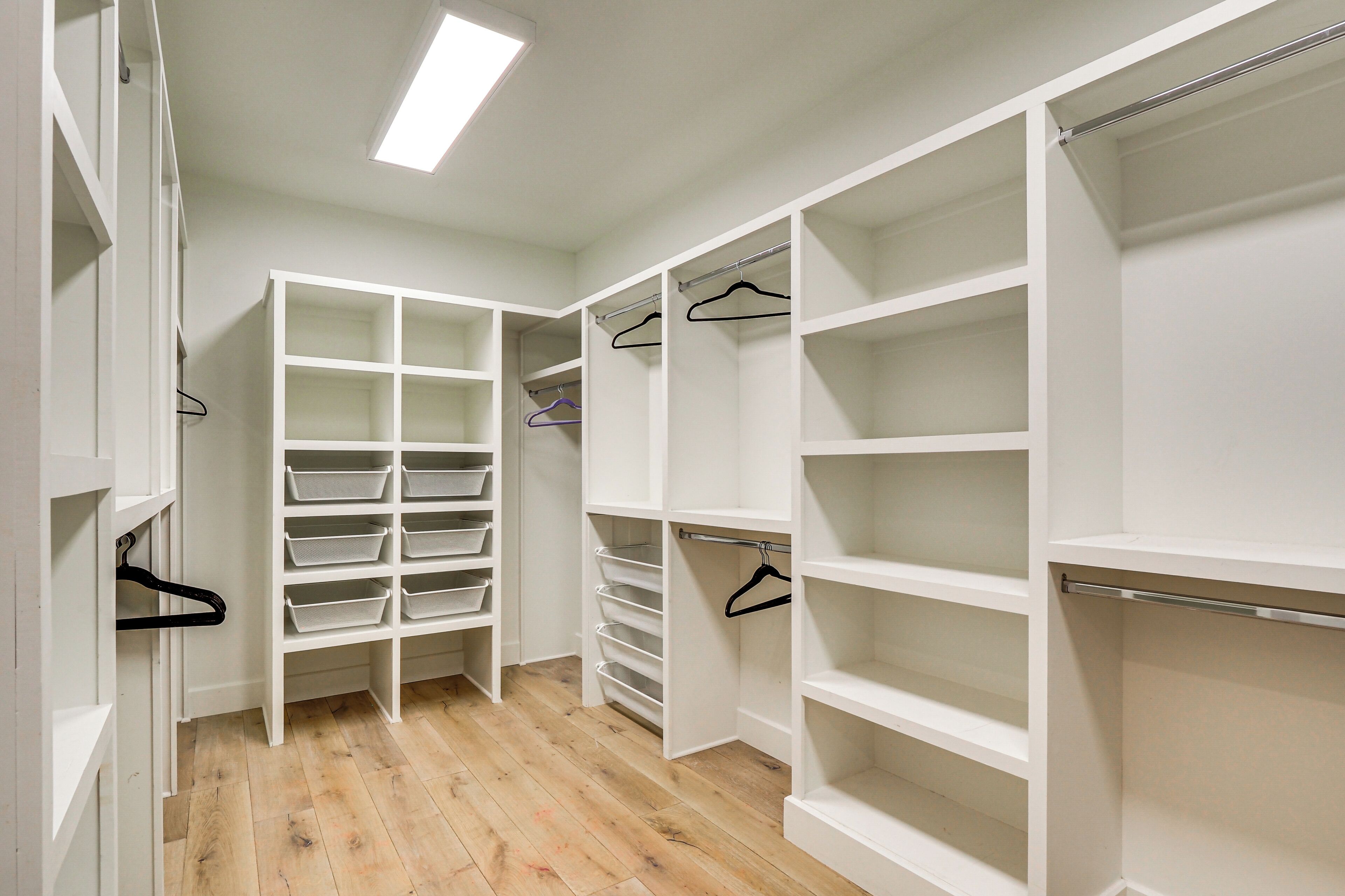 Un vestidor amplio con estantes y espacio para colgar, suelo de madera y un tragaluz.
