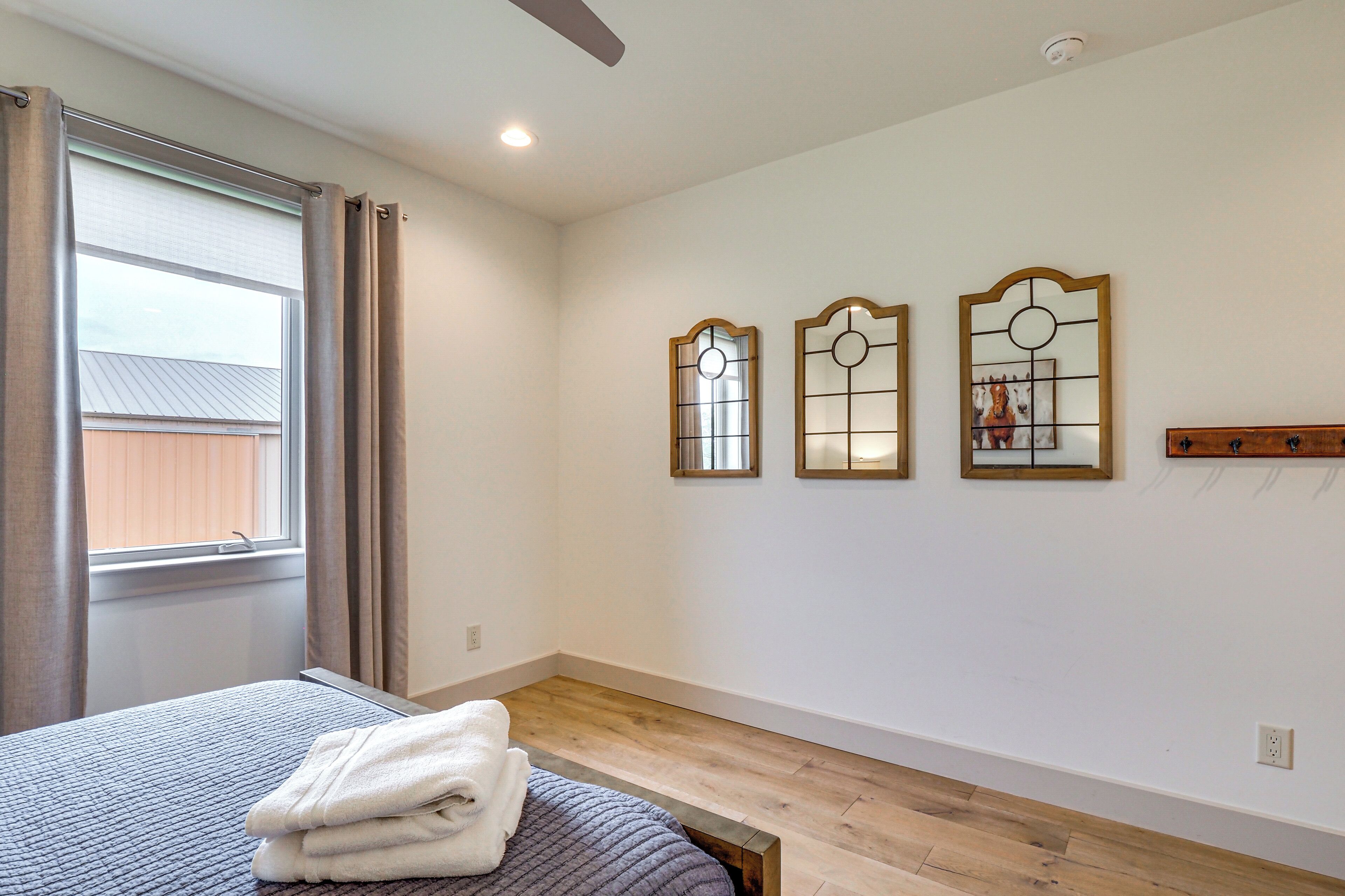 A bedroom with a bed, a window with curtains, and three wall-mounted mirrors.