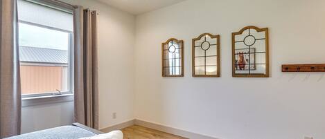 A bedroom with a bed, a window with curtains, and three wall-mounted mirrors.