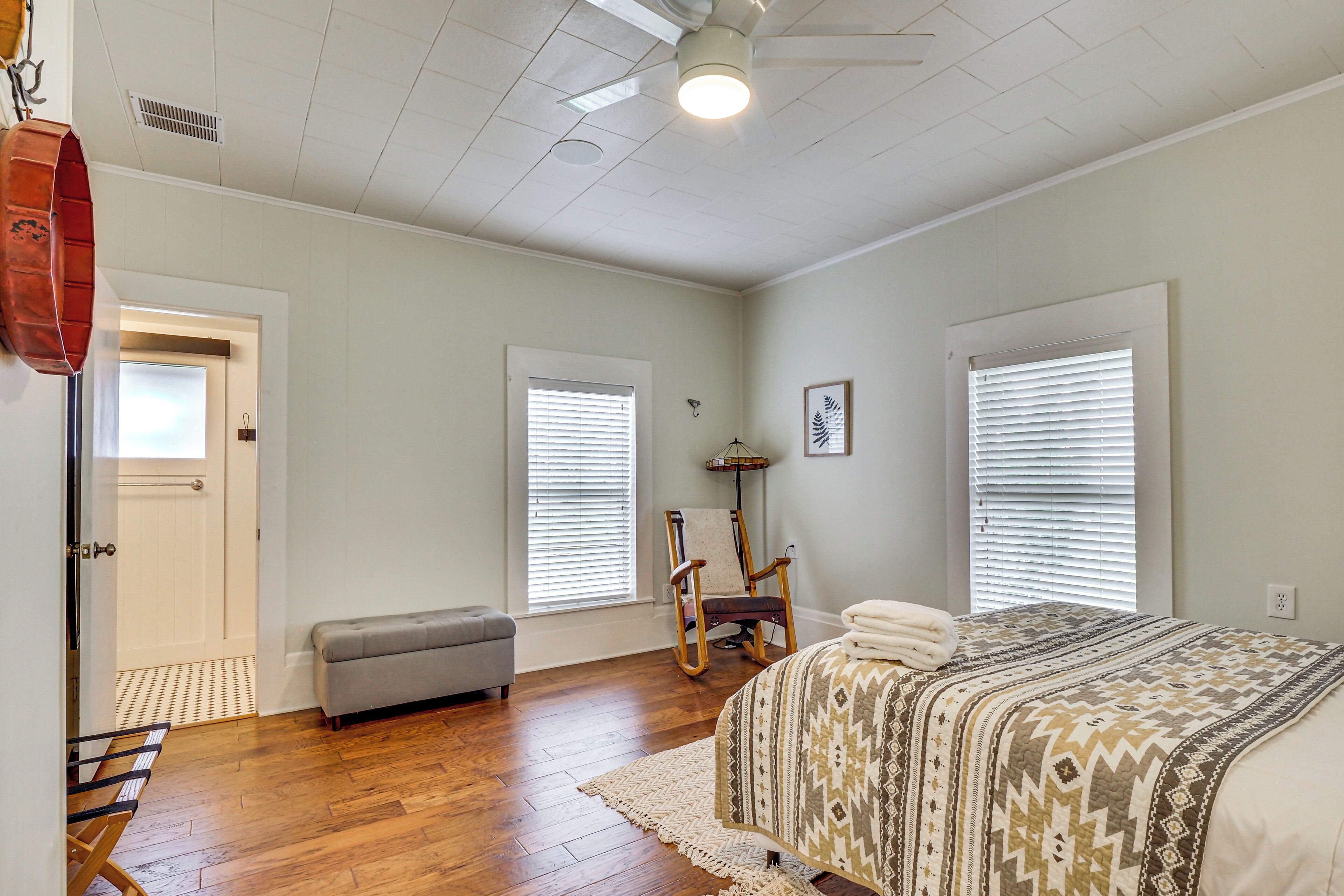A bedroom with a bed, a bench, a rocking chair, and a door.