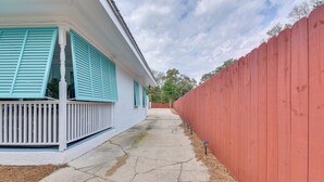 A narrow concrete pathway flanked by a white building with teal shutters and a red wooden fence. - Fort Walton Beach Bungalow w/ Private Hot Tub! (Fort Walton Beach)