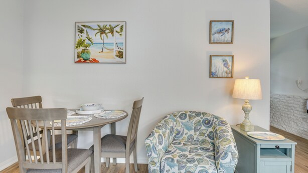 A dining area with a round table, two chairs, and a patterned armchair. There are framed artworks on the wall and a lamp on a side table. - Fort Walton Beach Bungalow w/ Private Hot Tub! (Fort Walton Beach)