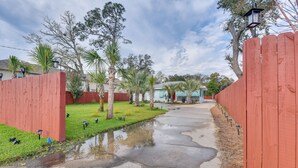 A residential street with a red fence, a small puddle, and houses in the background. - Fort Walton Beach Bungalow w/ Private Hot Tub! (Fort Walton Beach)