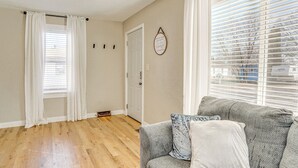 Un salón con un sofá gris, cojines blancos y una ventana con persianas.