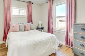 A bedroom with a bed, a dresser, a nightstand, a lamp, and a window with curtains. - Pet-friendly Watertown Home ~ 1 Mi to Downtown! (Watertown)