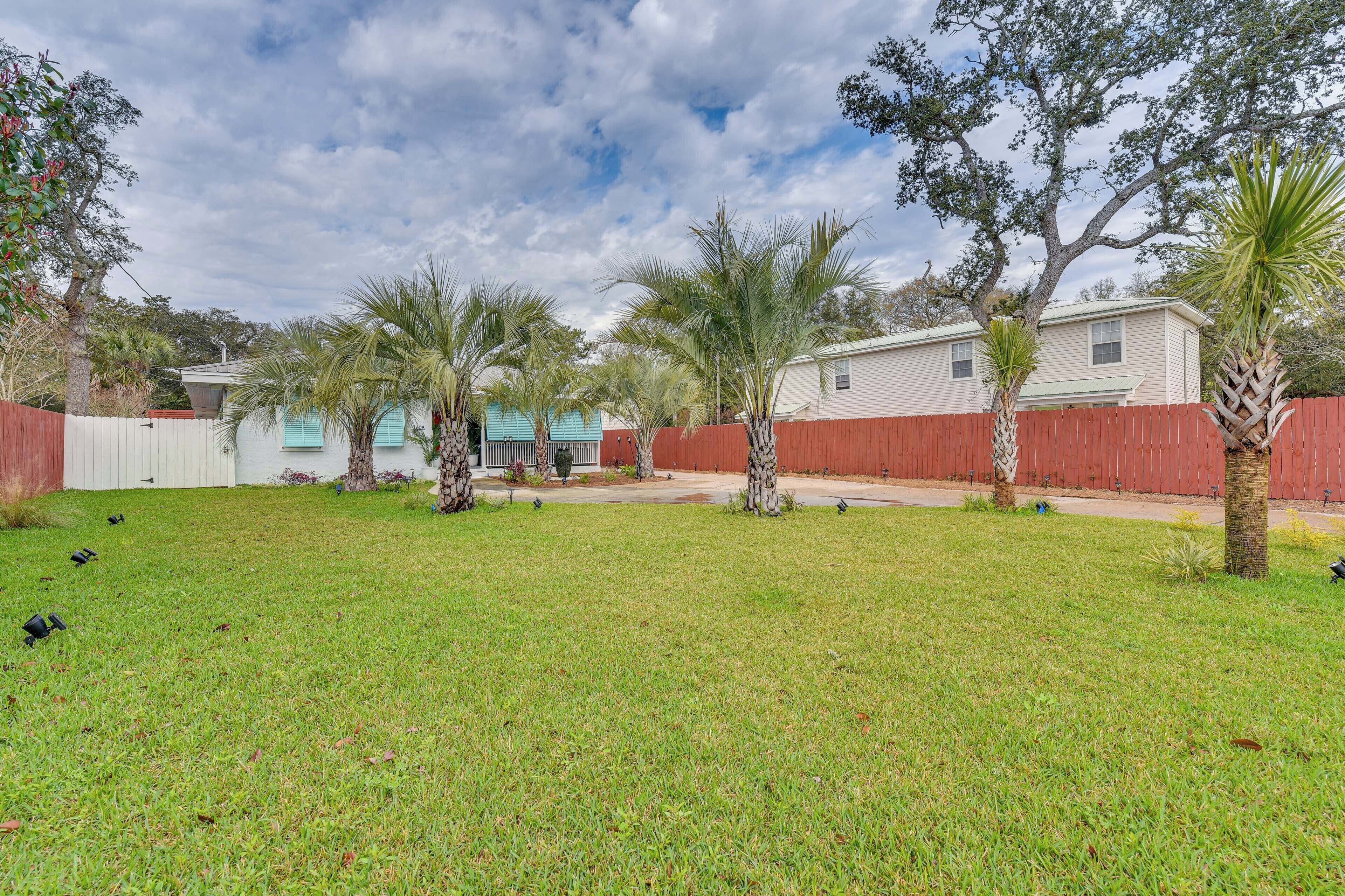 A backyard with a lawn, palm trees, a red fence, and a house with a white exterior.