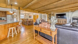 Cozinha ampla com vigas de madeira, área de jantar com lustre e sala de estar com sofá de couro e objetos decorativos.