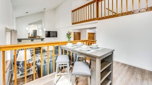 Een eetruimte met een houten tafel voor vier personen, een trap met houten leuningen, en een keuken op de achtergrond.