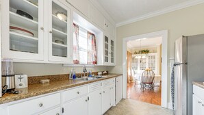 A kitchen with white cabinets, a granite countertop, a stainless steel refrigerator, and a dining area visible through an open doorway. - Sanford Vacation Rental ~ 1 Mi to Downtown! (Sanford)