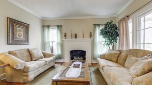 A living room with two beige sofas, a wooden coffee table, a fireplace, and a large plant. - Sanford Vacation Rental ~ 1 Mi to Downtown! (Sanford)