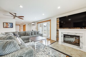 A living room with a sectional sofa, a coffee table, a fireplace, and a flat-screen TV. - Spacious Presque Isle Home: Walk to Downtown! (Presque Isle)