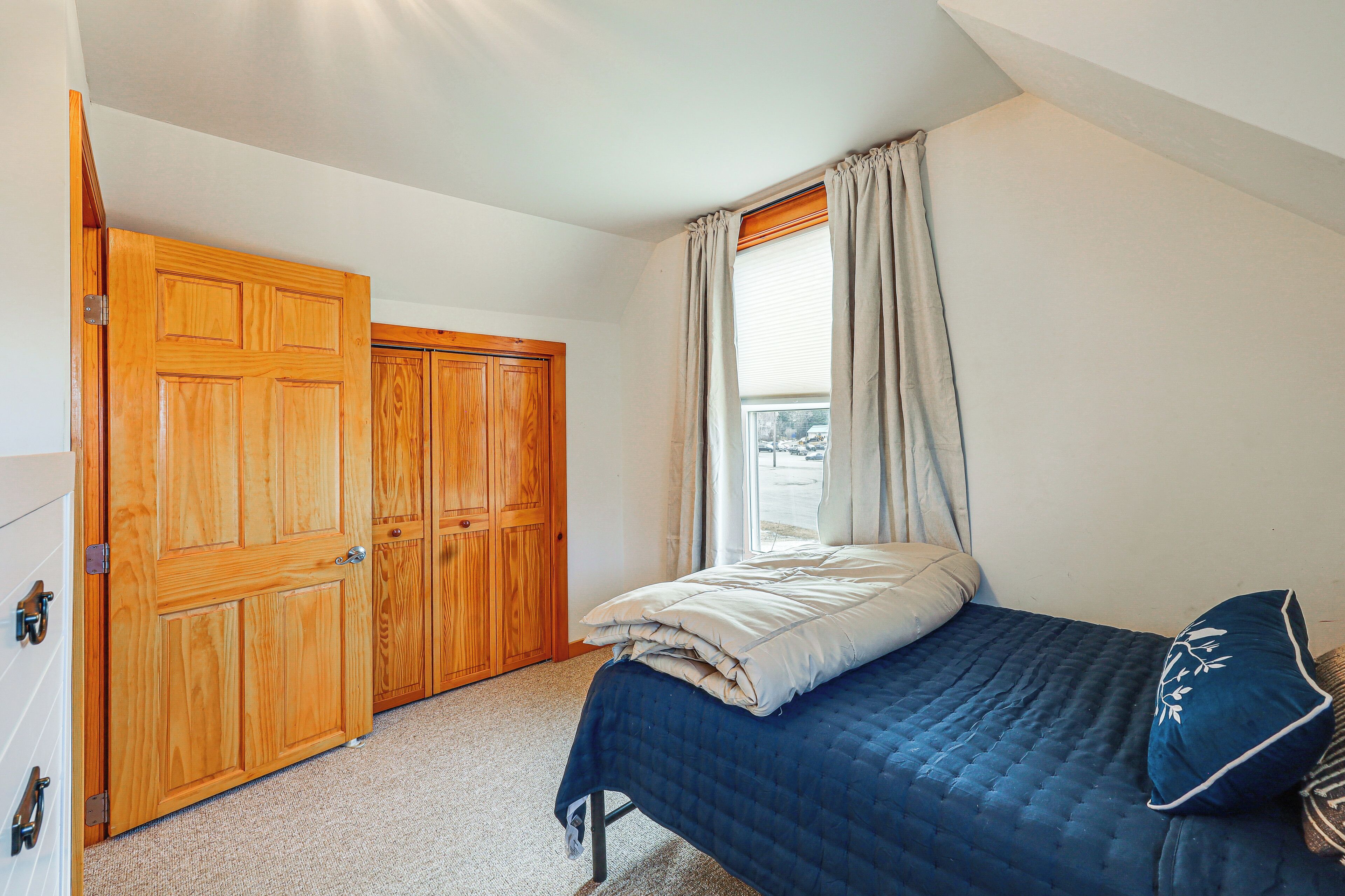 Une chambre à coucher avec un lit, une fenêtre avec des rideaux et des armoires en bois.